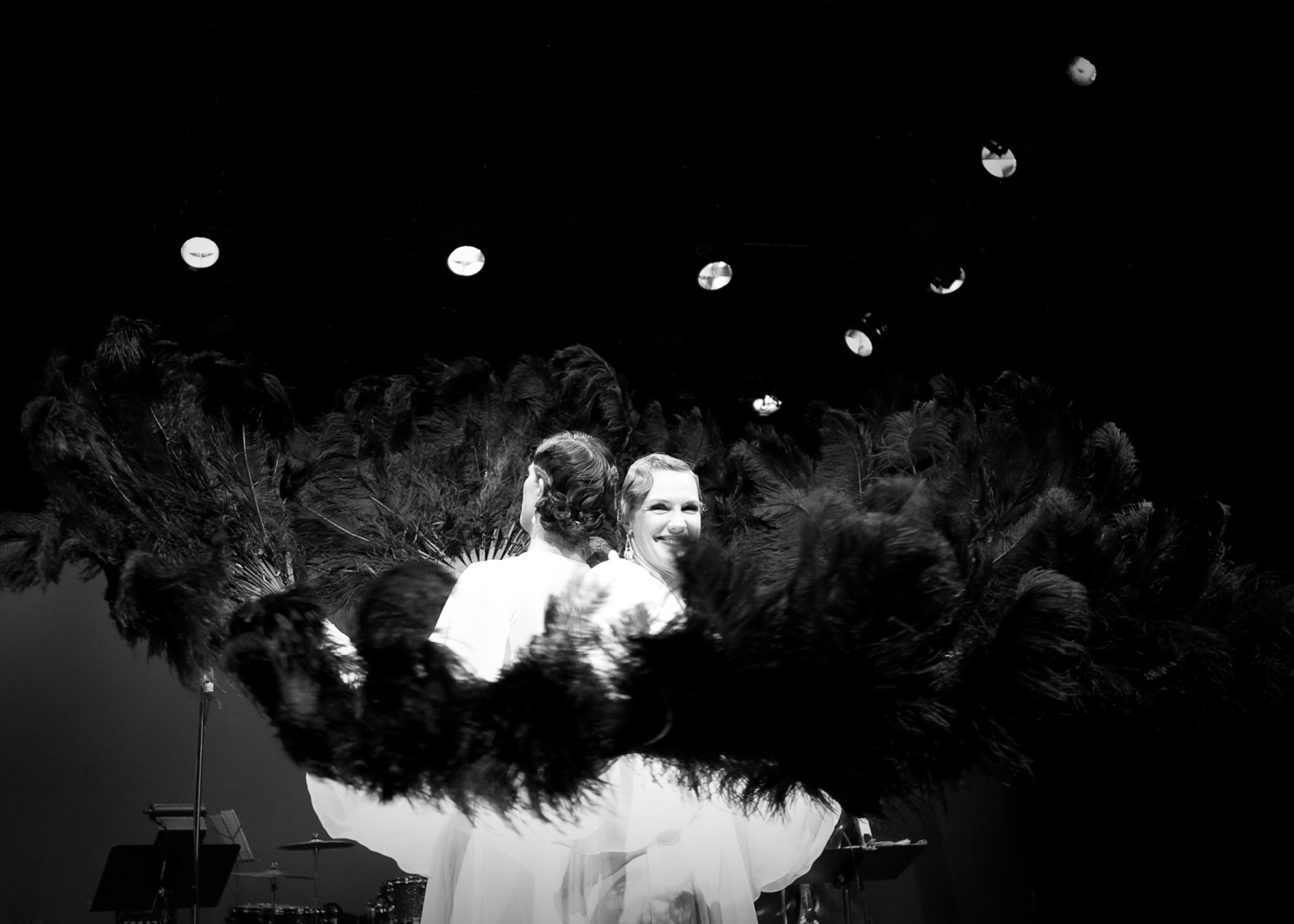 Dancers holding black ostrich feather fans in a circle on stage.